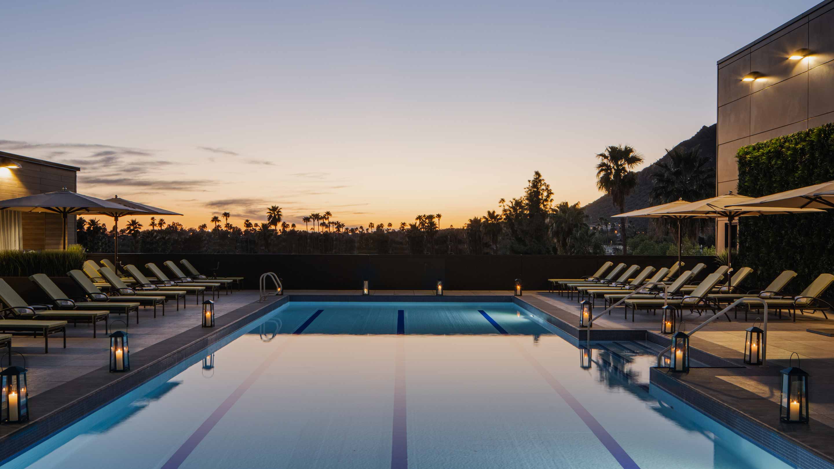 A 3 lane pool, surrounded by lounge chairs, at dusk