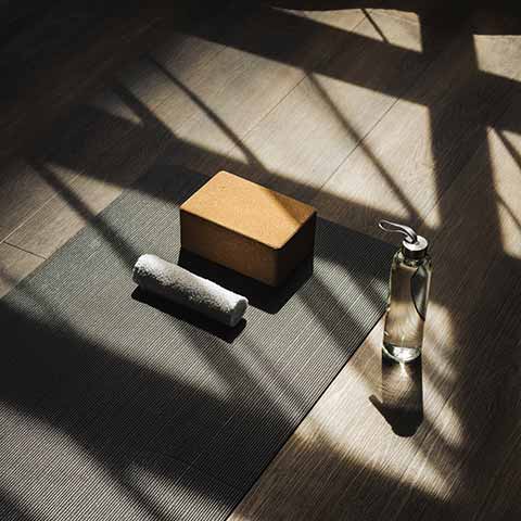 A yoga mat, towel, and water bottle striped with shadows from the morning sun