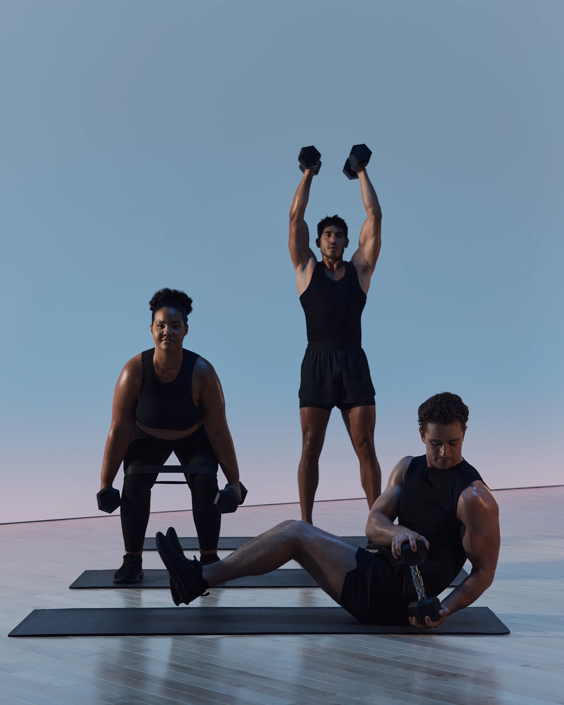 A group of three people in different poses working out with dumbbells in a maxout strength class