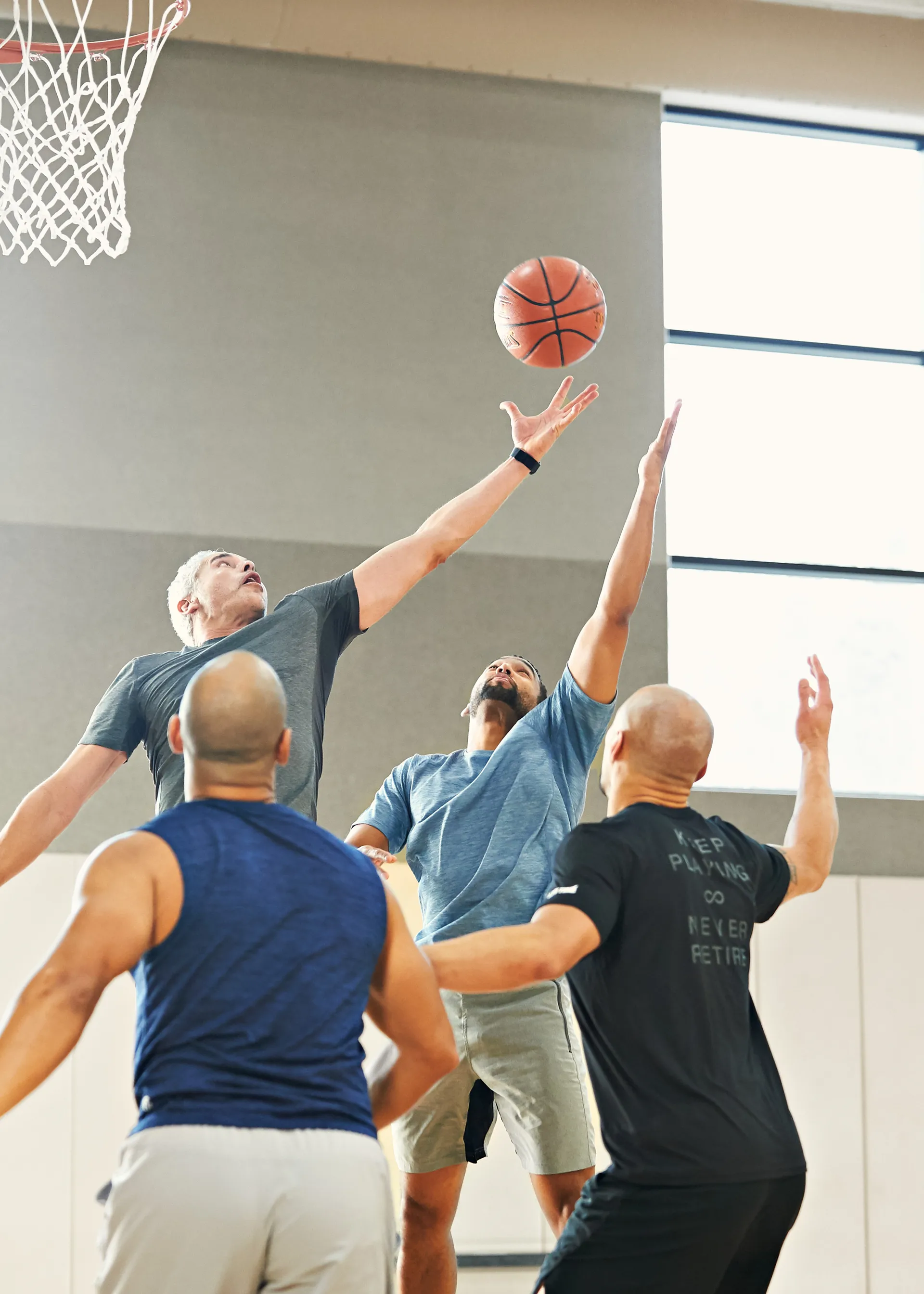 Four men playing basketball in an indoor gym where one player is jumping for the ball.