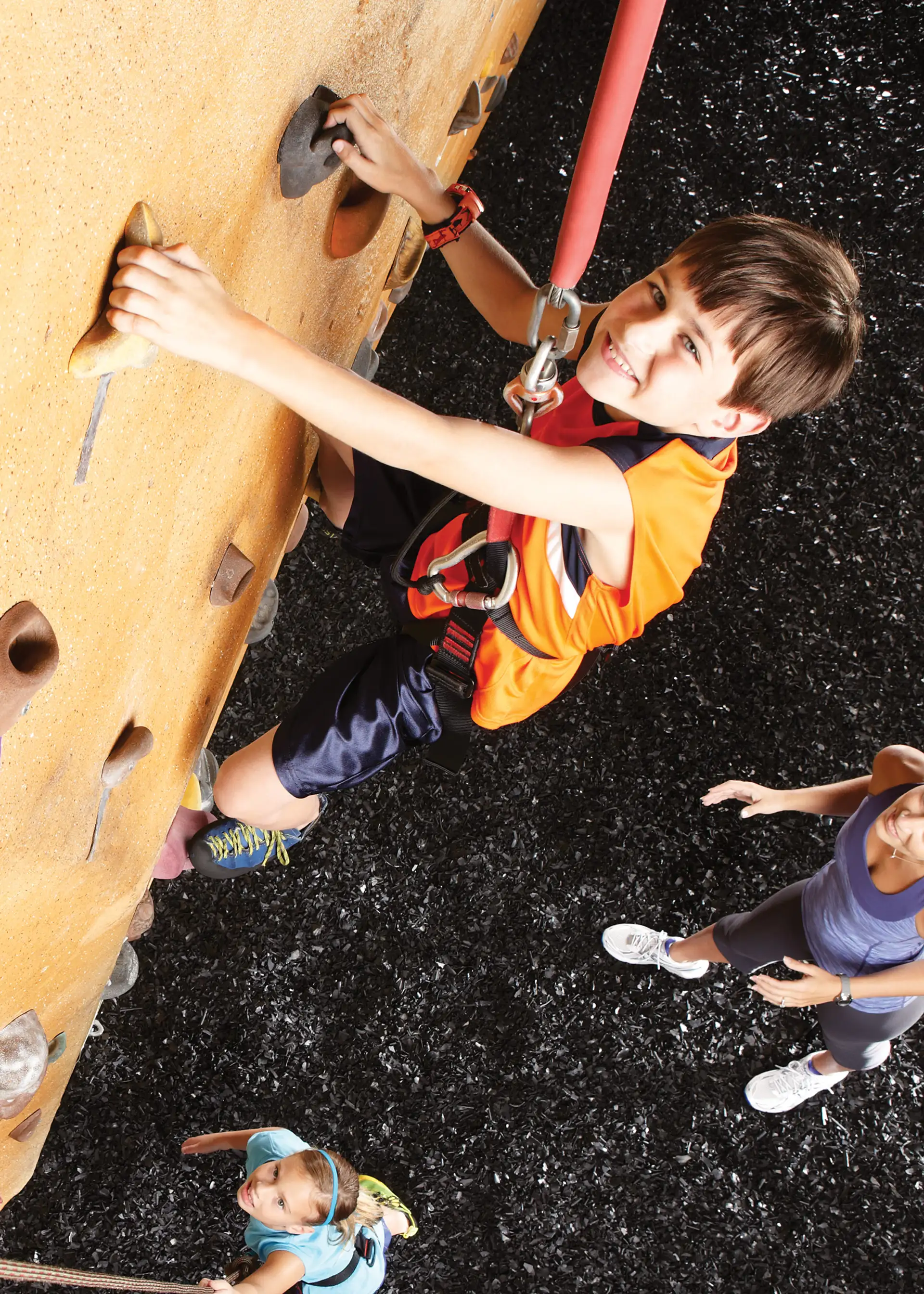 A smiling kid in a harness climbing on a rock wall