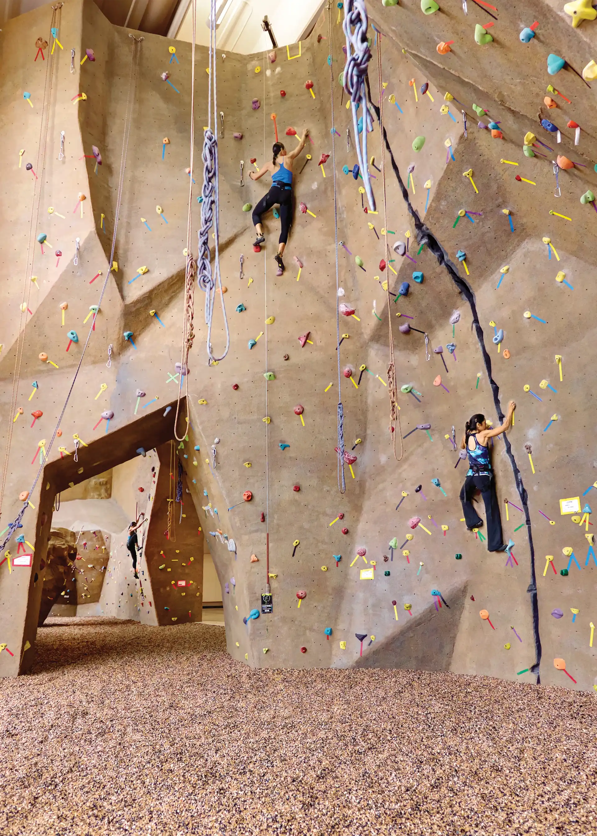 Two people in harnesses climbing on an indoor rock wall.