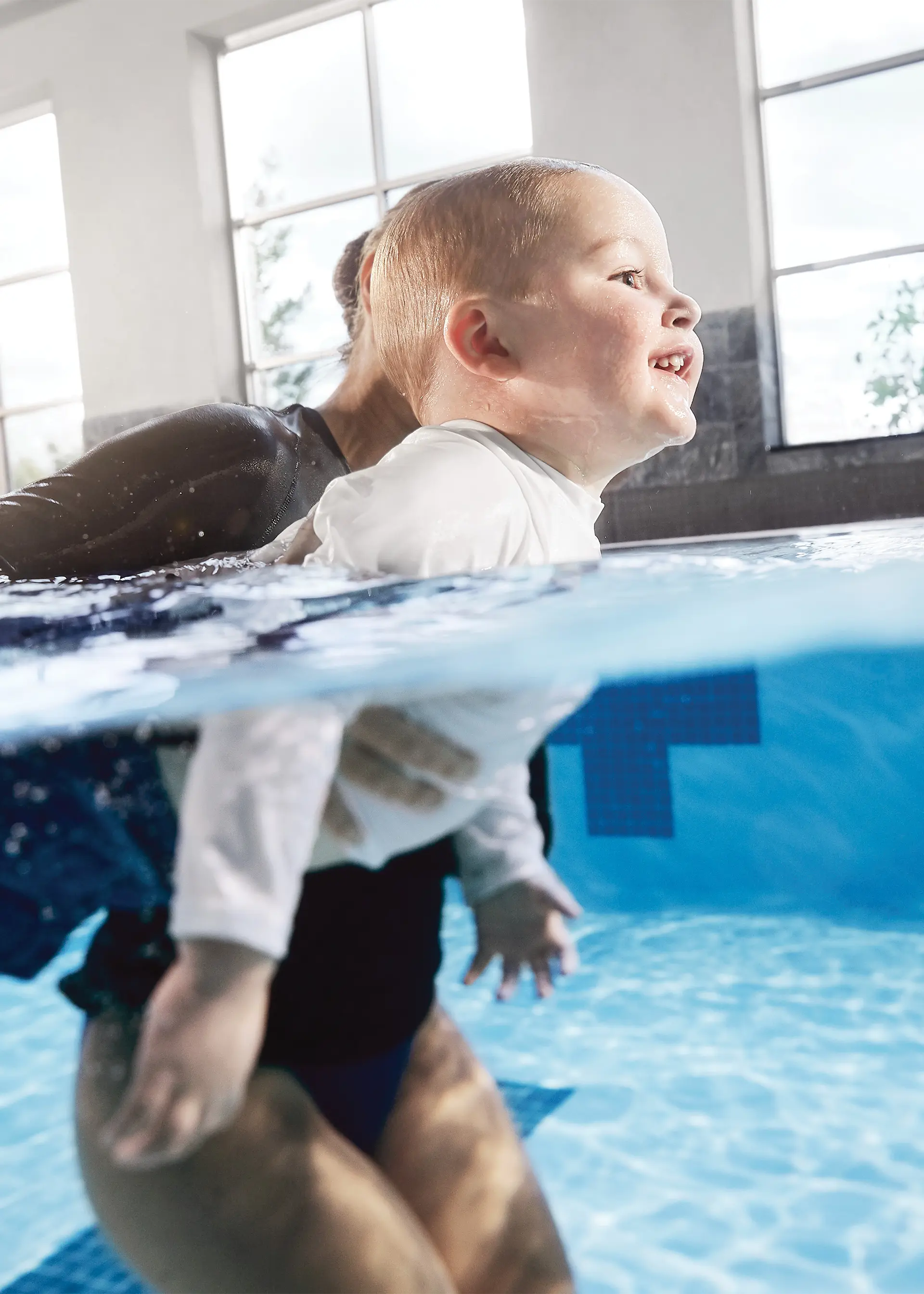 A child swimming in an indoor pool assisted by an adult.