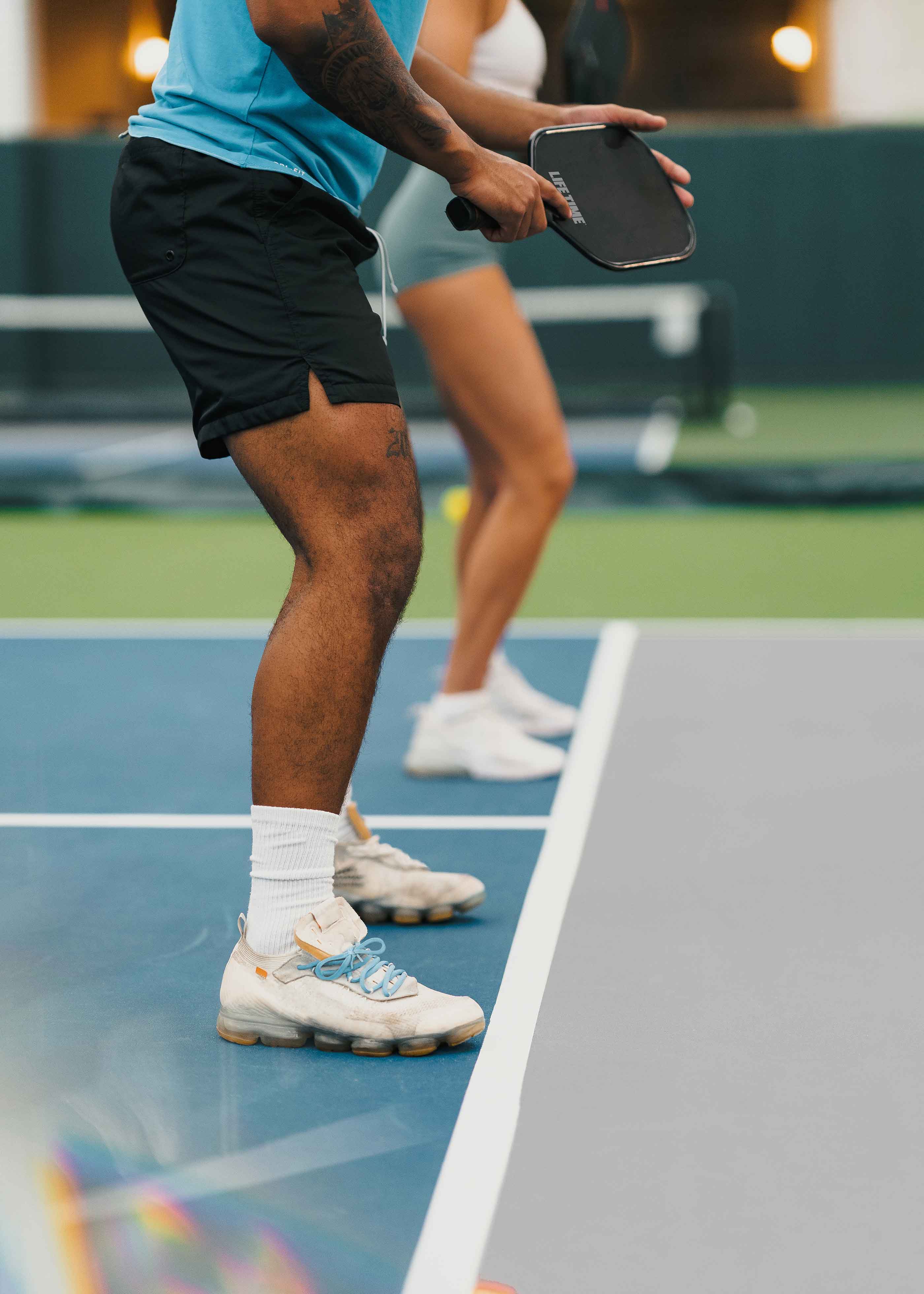 Two pickleball players stand ready on a pickleball to play a doubles game