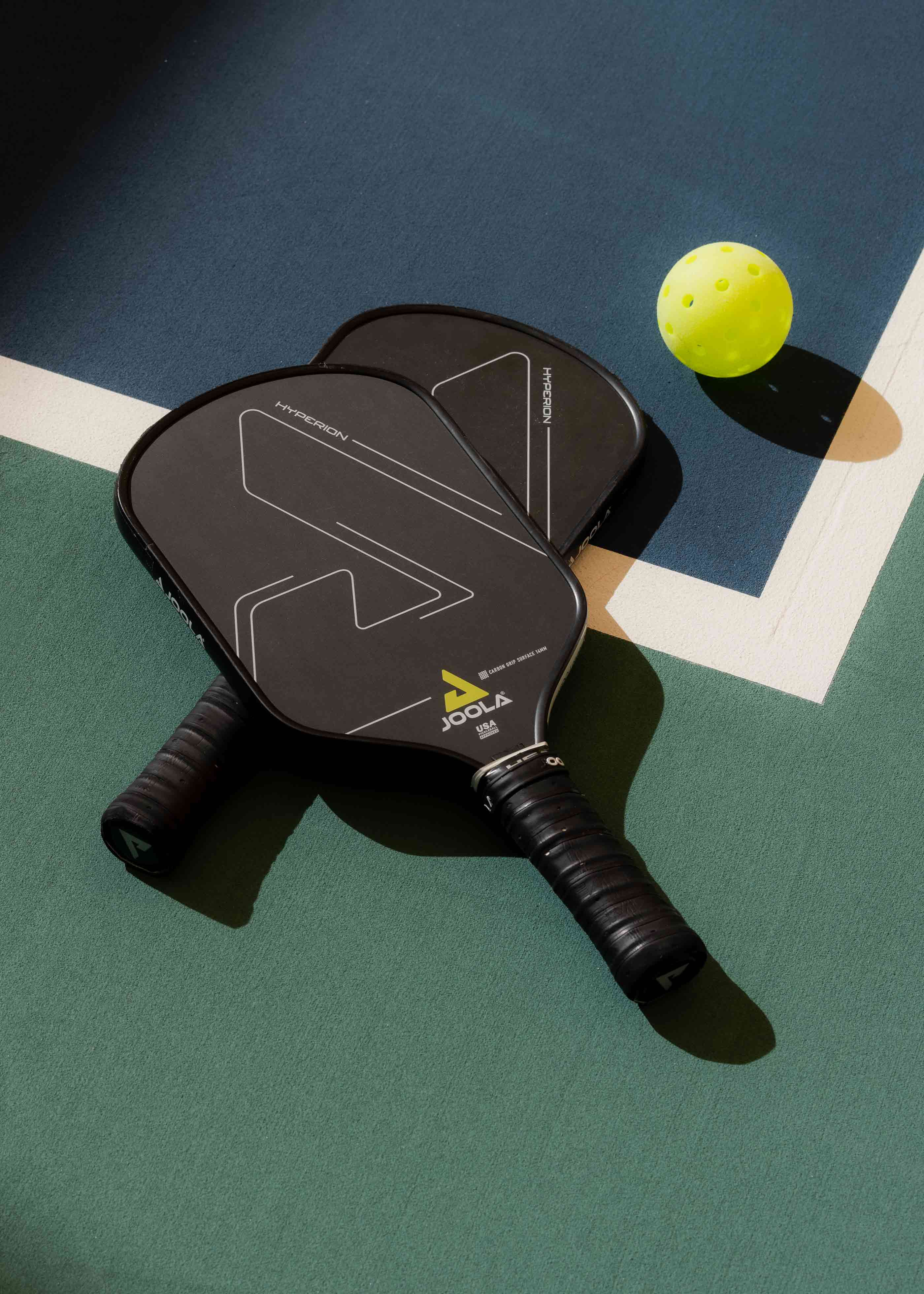 Two pickleball paddles and a ball laying on a pickleball court