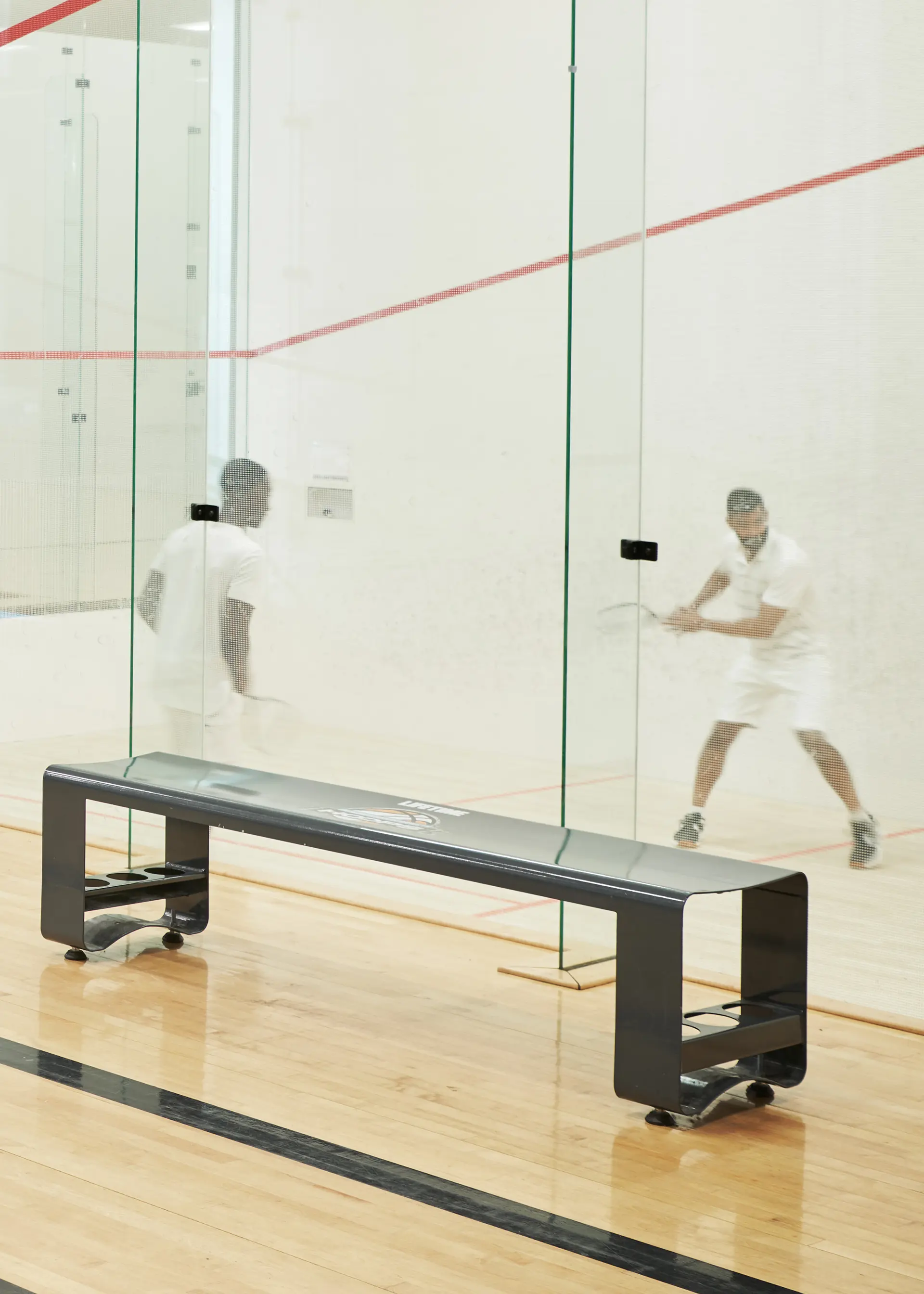 Two people holding racquets and playing squash on an indoor court.