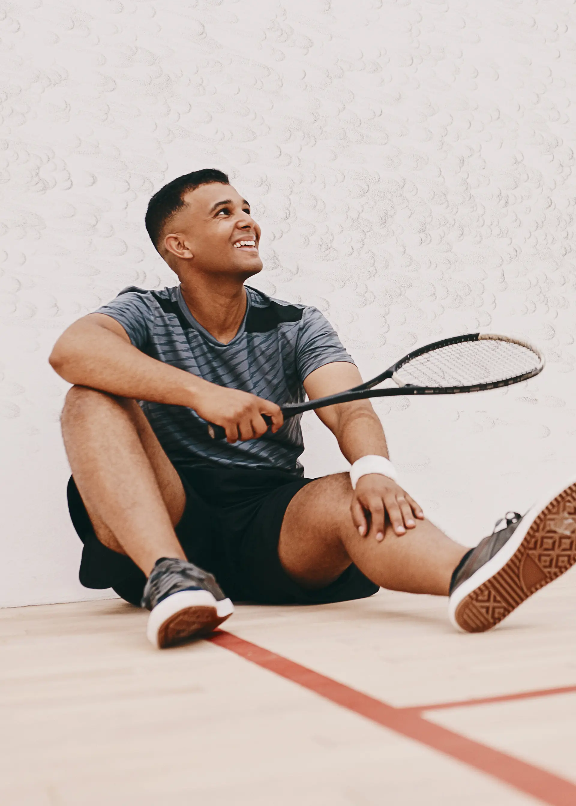 A male squash player sitting and holding a racquet