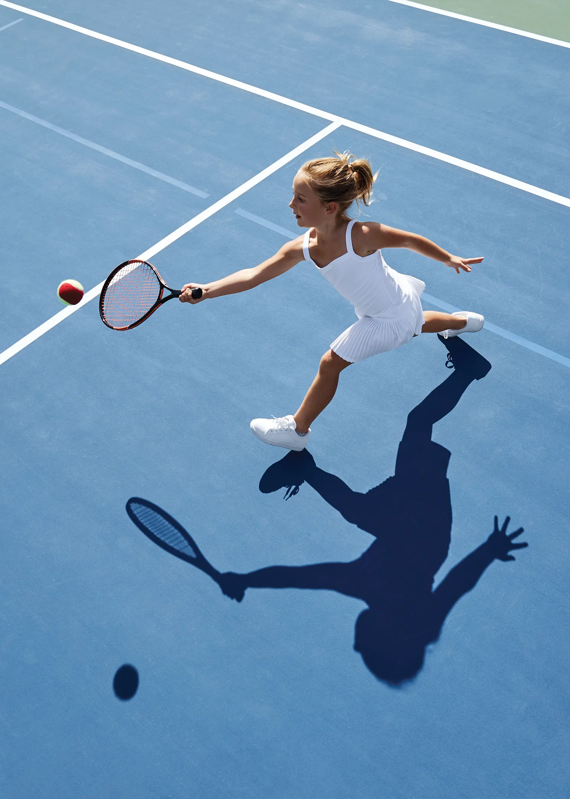 A person on a tennis court wearing white clothing and shoes holding a racket and reaching to hit a tennis ball.