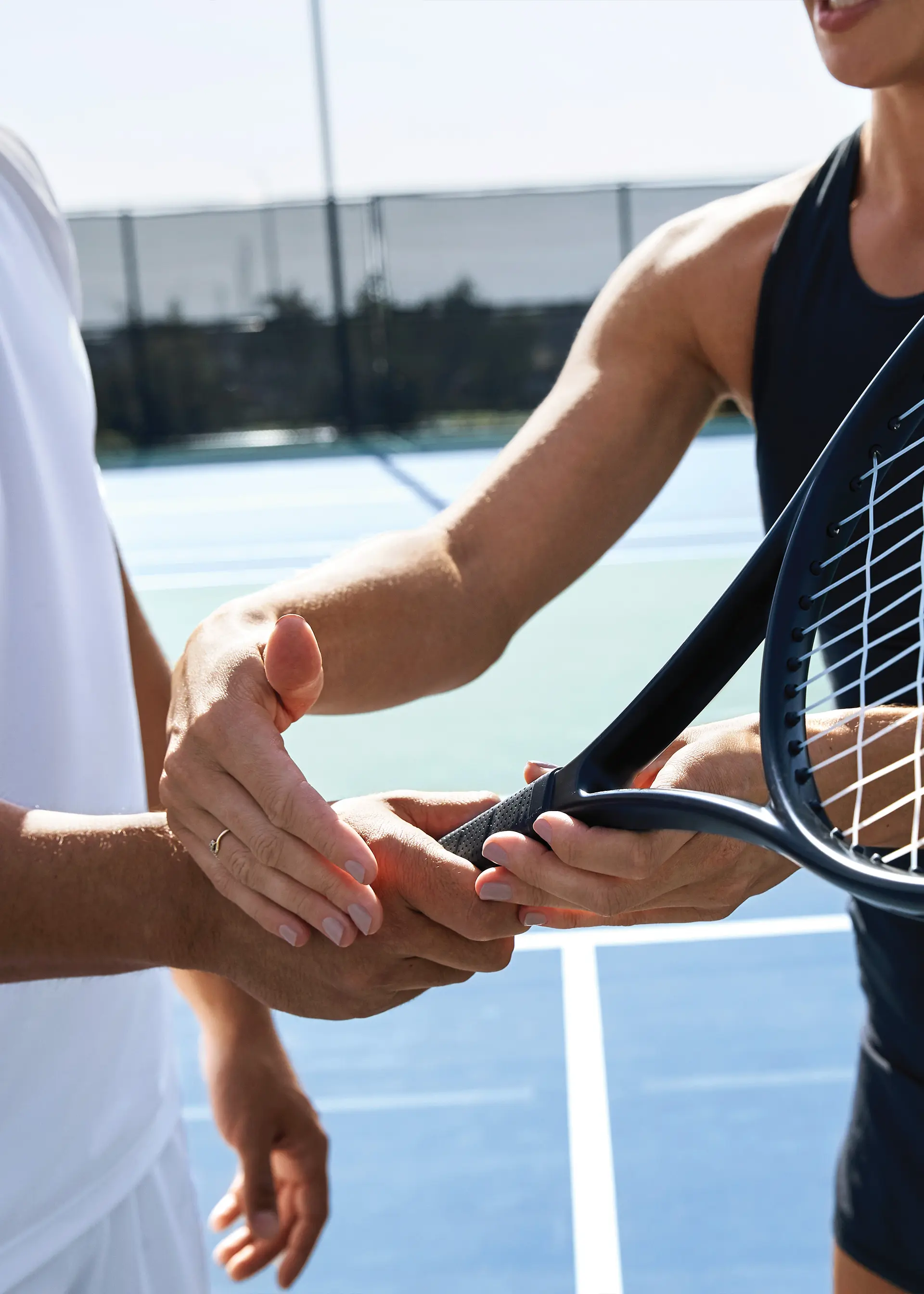Two people holding a tennis racket on an outdoor court