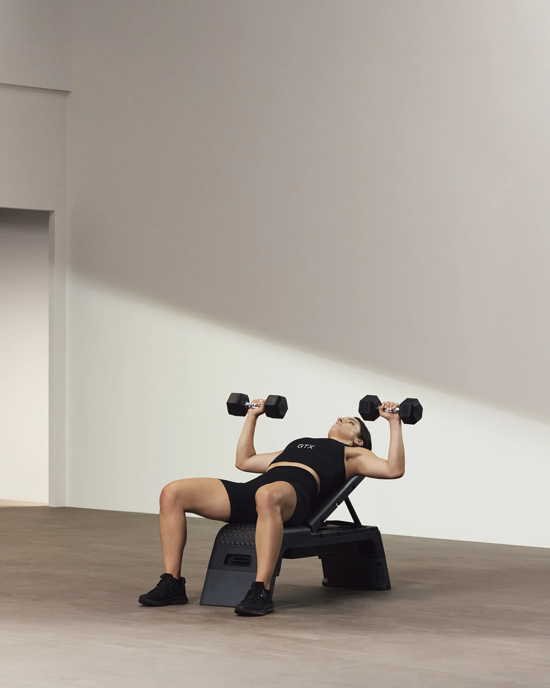 A Life Time member holding two dumbbells on an incline bench.