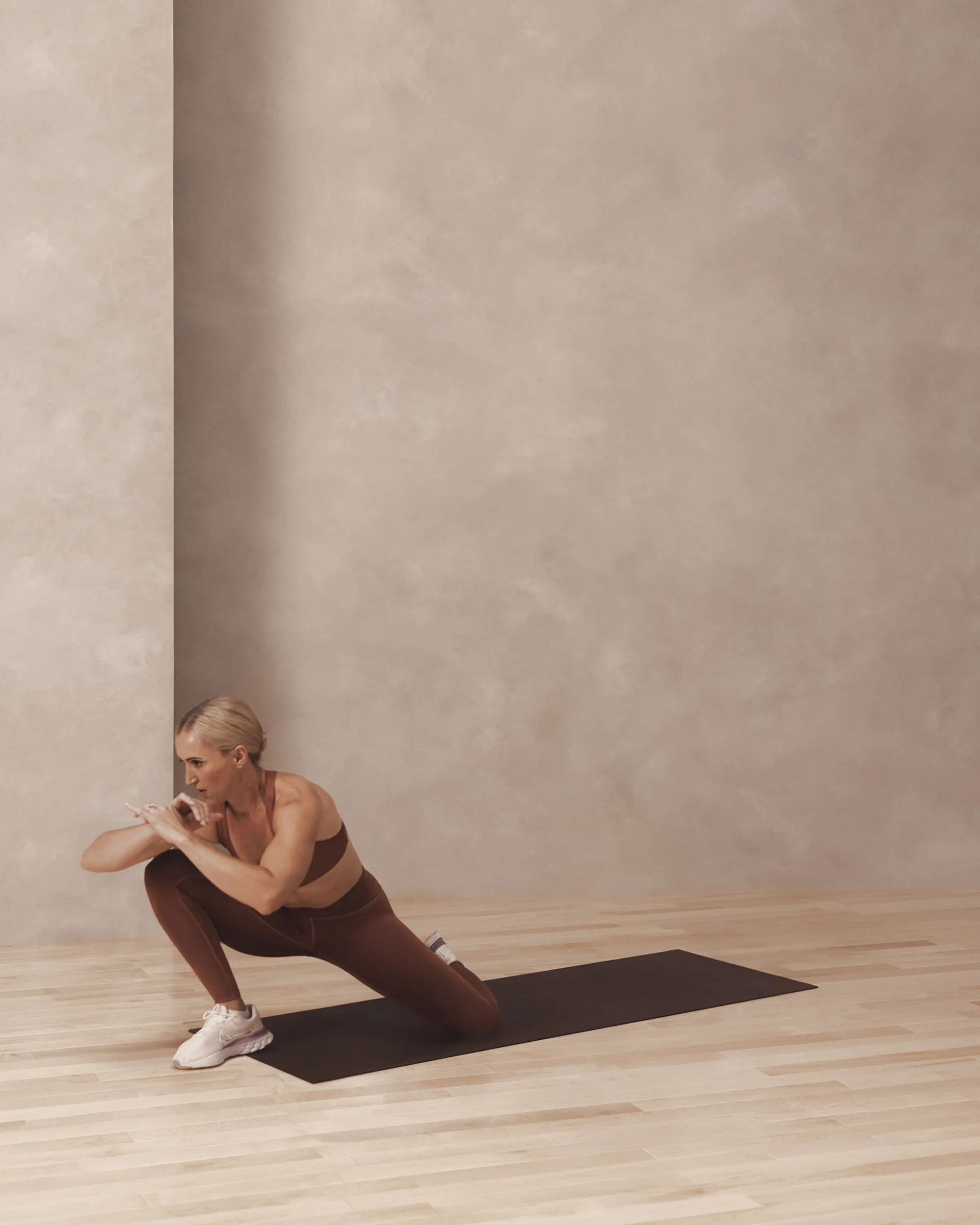A Life Time member lunging on one knee on a yoga mat.
