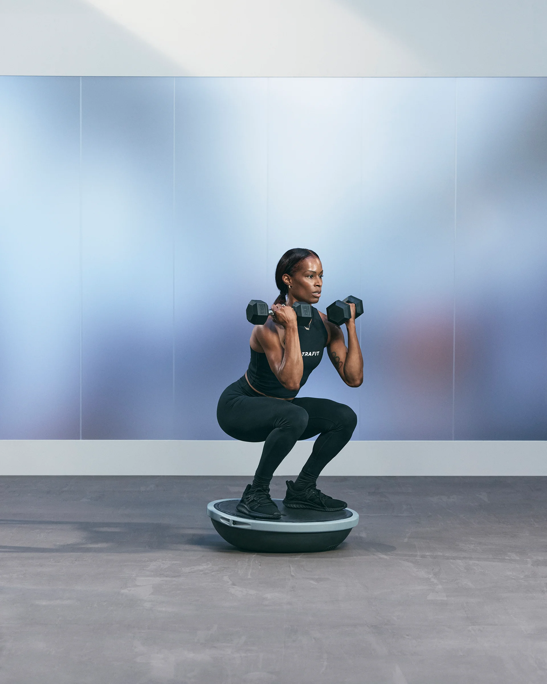 A Life Time member squatting on a bosu ball and holding dumbbells.