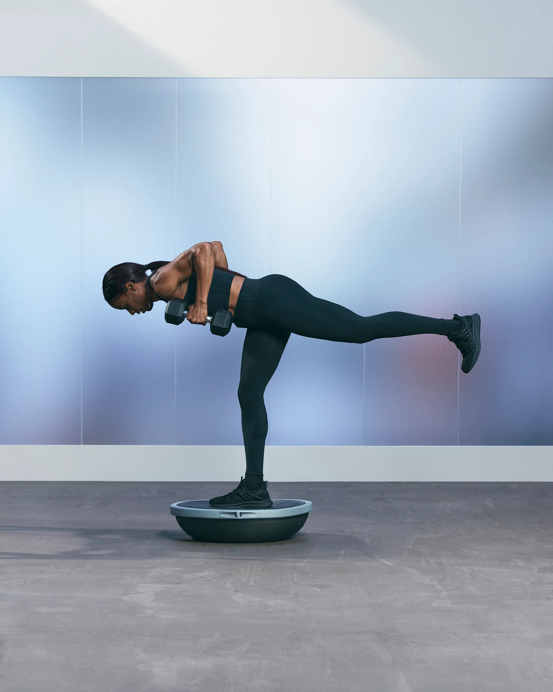A Life Time member balancing on one leg using a BOSU while holding dumbbells.