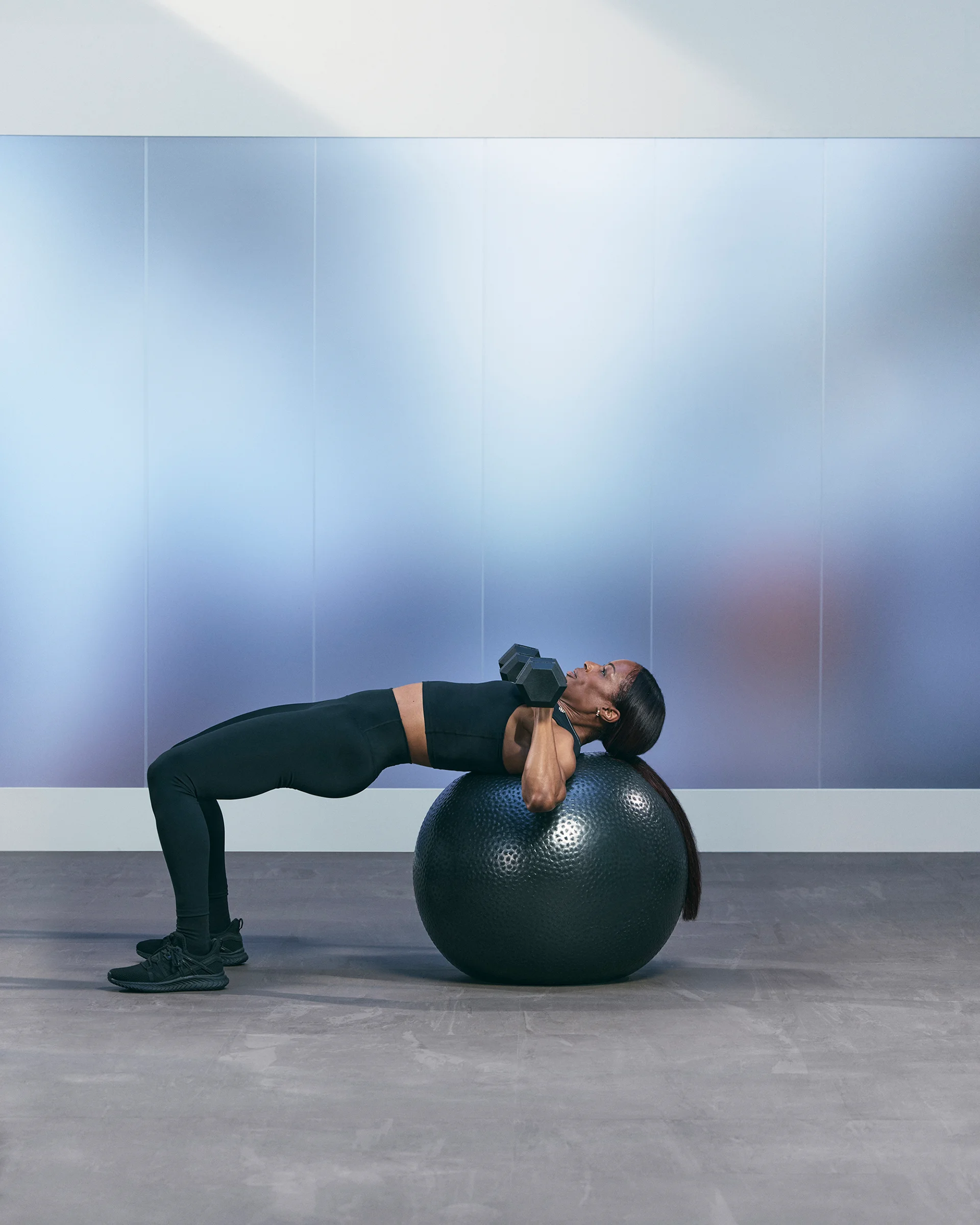 A Life Time member in a table top pose with a stability ball while doing a chest press with dumbells.