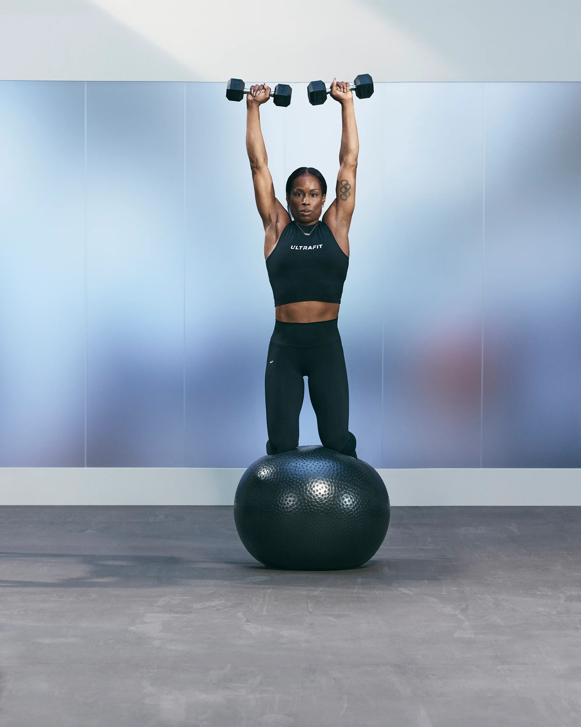 A Life Time member raising dumbbells overhead while kneeling on a stability ball.