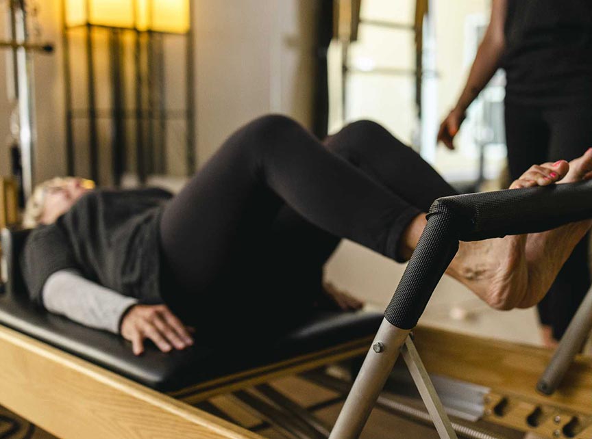 A Life Time personal trainer helps an woman on a pilates reformer machine.