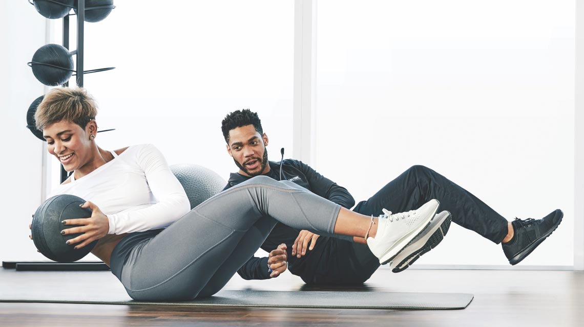 A trainer and a women doing an ab exercise with medicine balls