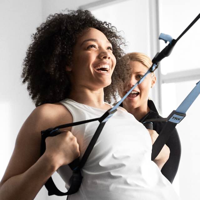 Two women in Life Time GTX class with personal trainer in background.