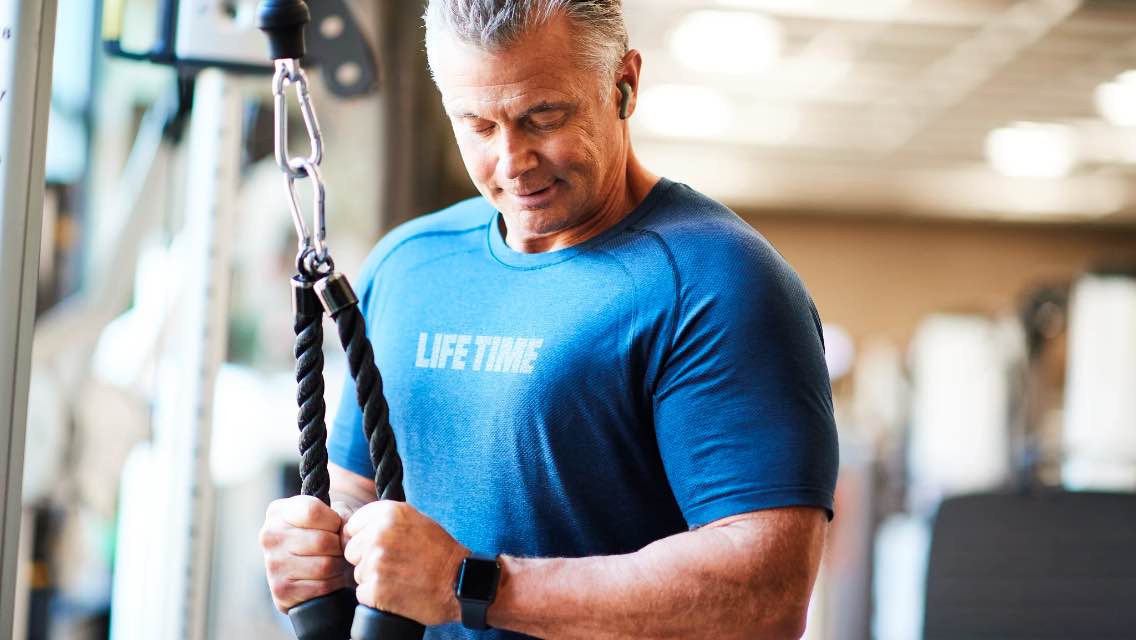 Image of man wearing Life Time shirt performing exercise in club. 