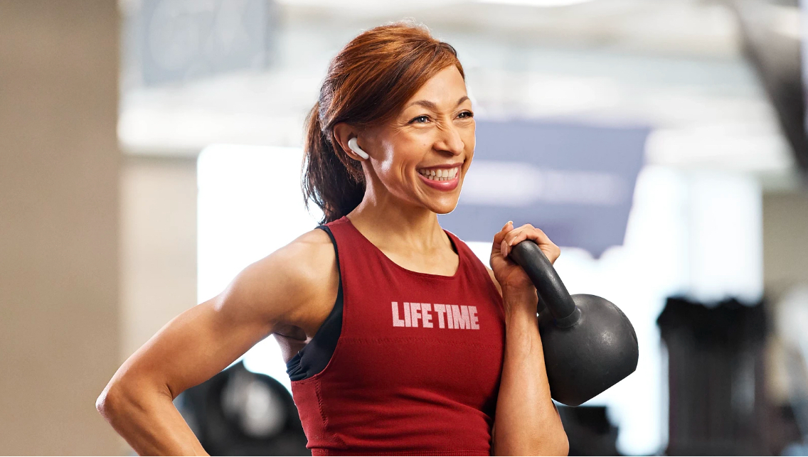 Image of woman wearing Life Time shirt holding a kettlebell.