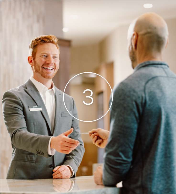 Man smiling at another man while they exchange a card.