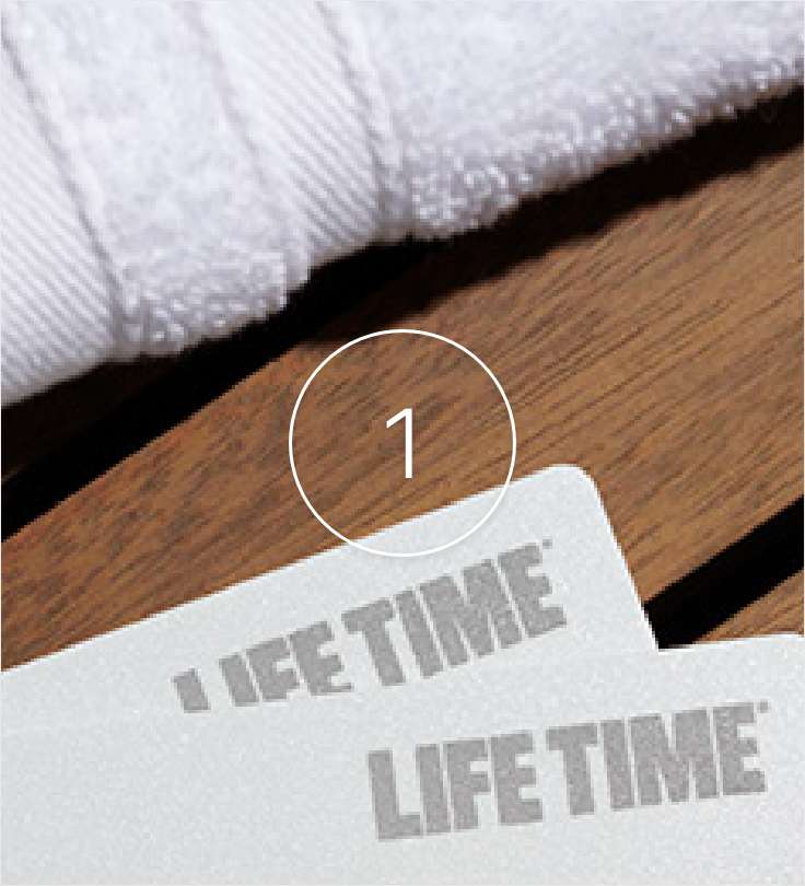A white Life Time access card sitting on a wooden bench with a white towel next to it.
