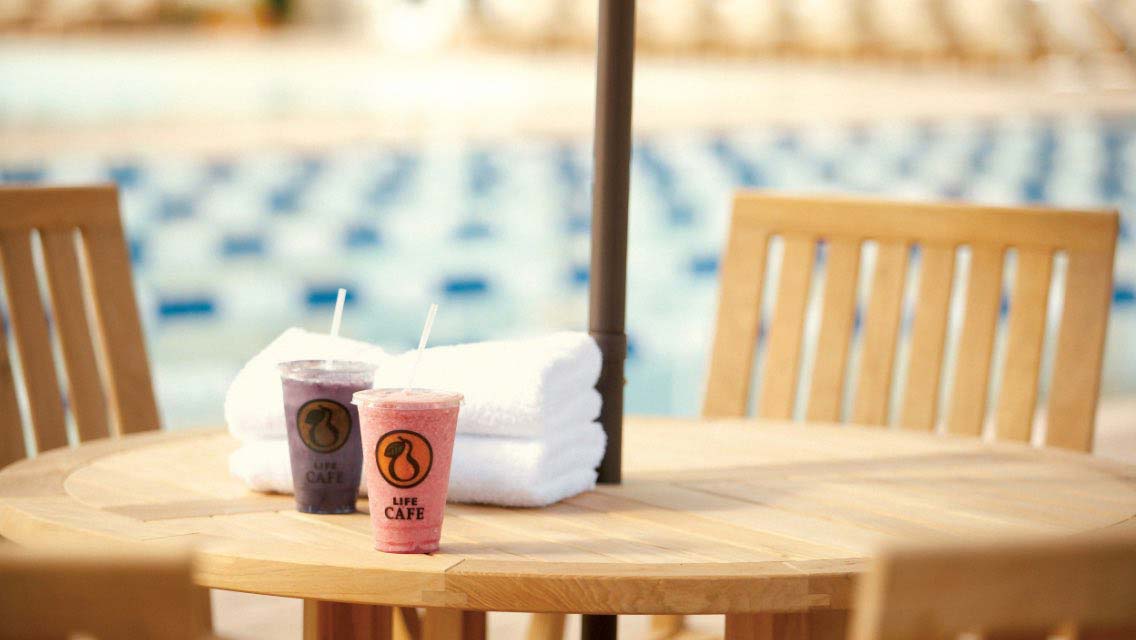 Two smoothies sitting on a poolside table at Life Time