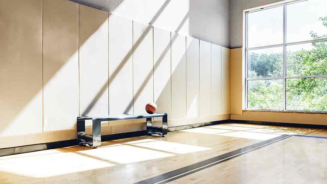 A basketball waits on a bench in a vacant, sunlit gym at Life time