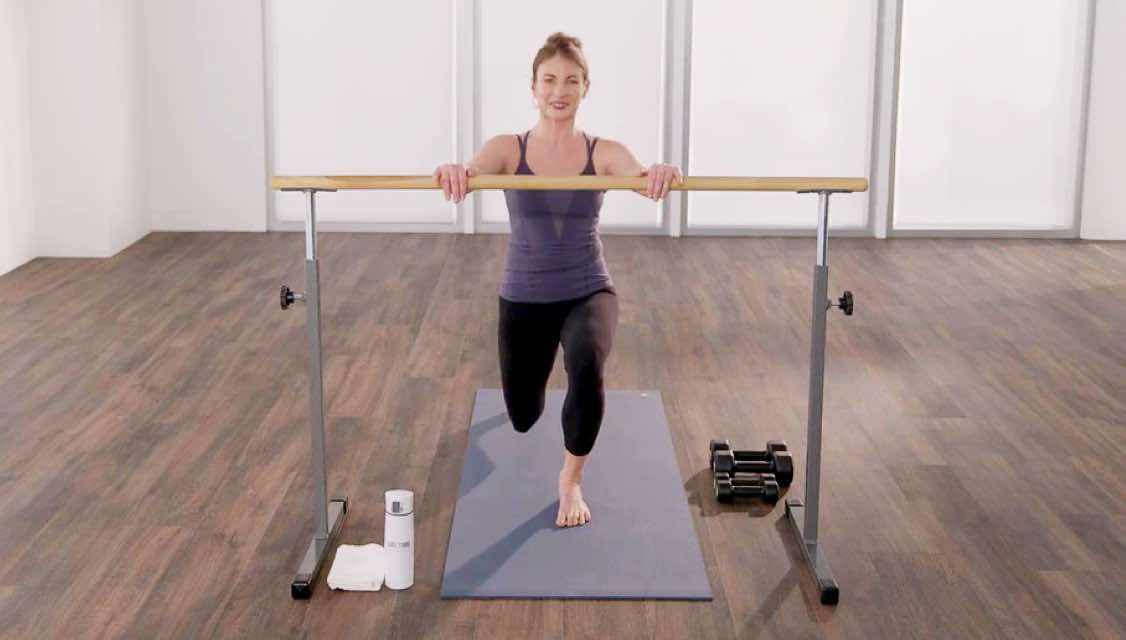 a woman prefors a barre move at a barre