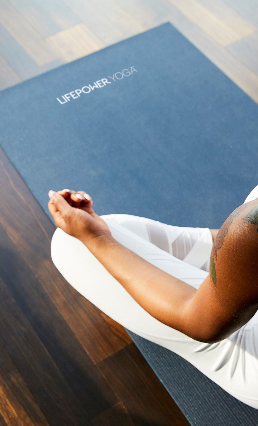 a woman sits with her legs folded on her yoga mat