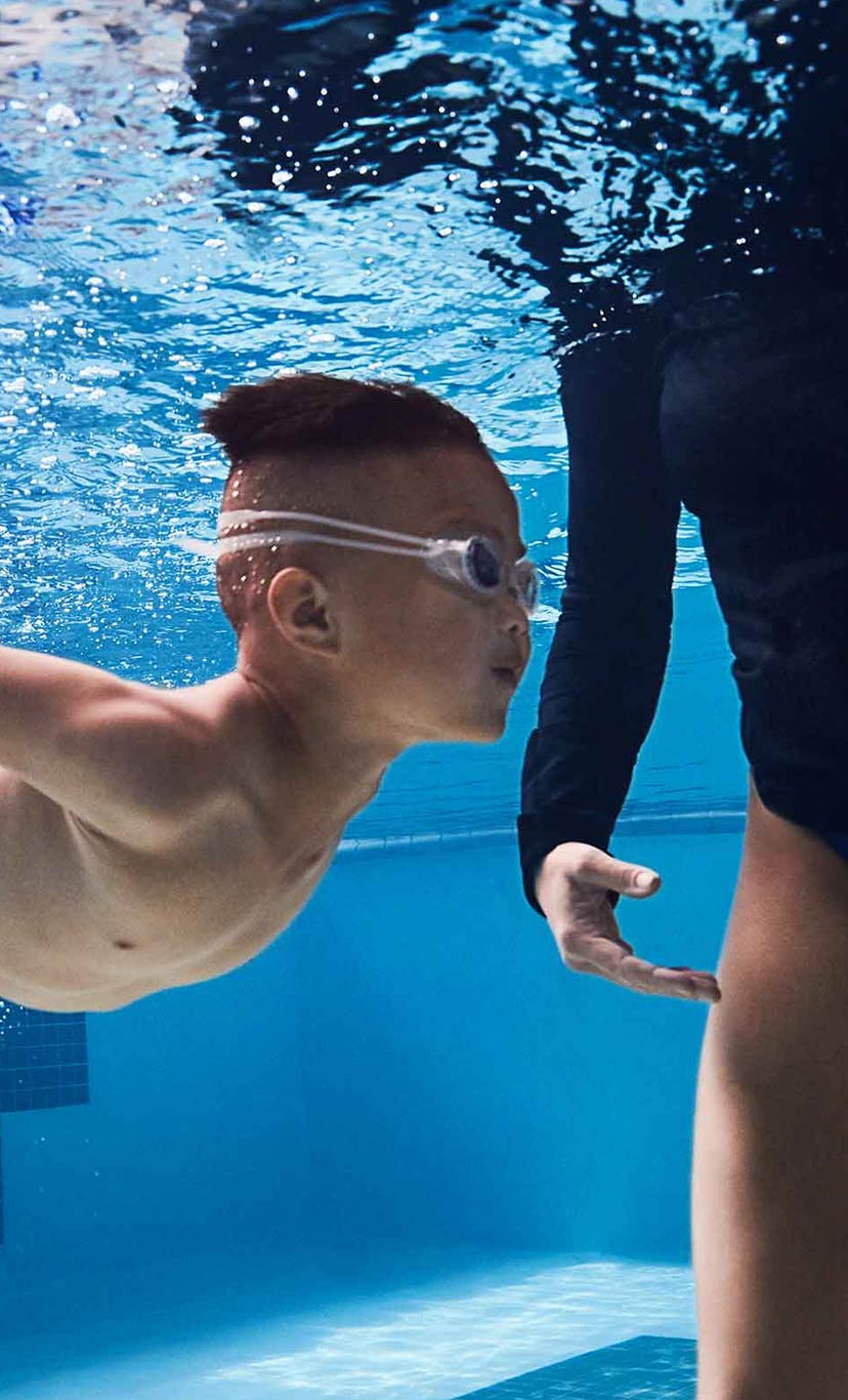 a young boy swims underwater toward an instructor