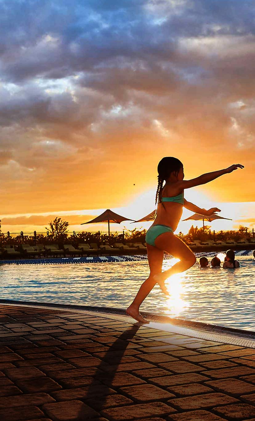 a girl jumps into an outdoor pool at dusk while her dad watches