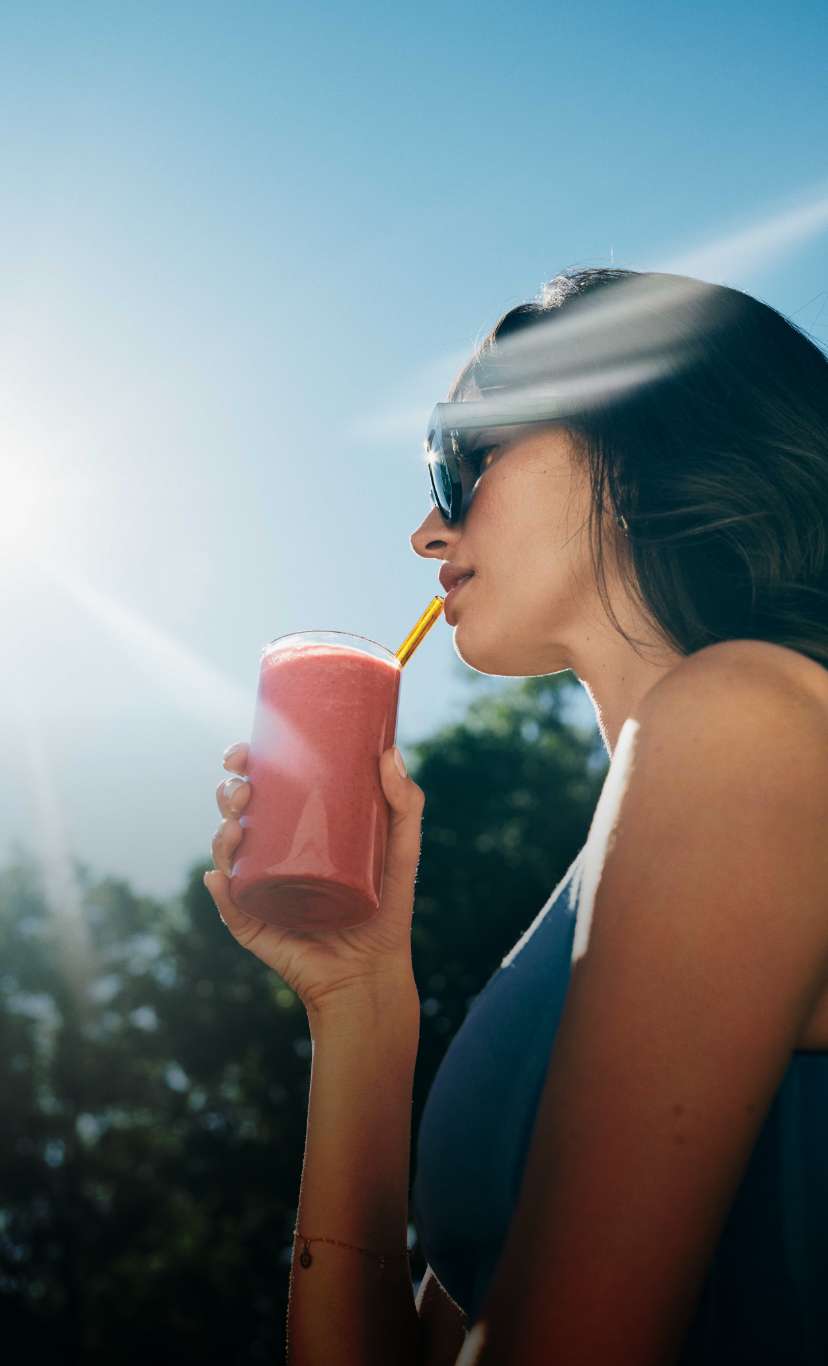 a woman sips on a smoothie in bright sunlight