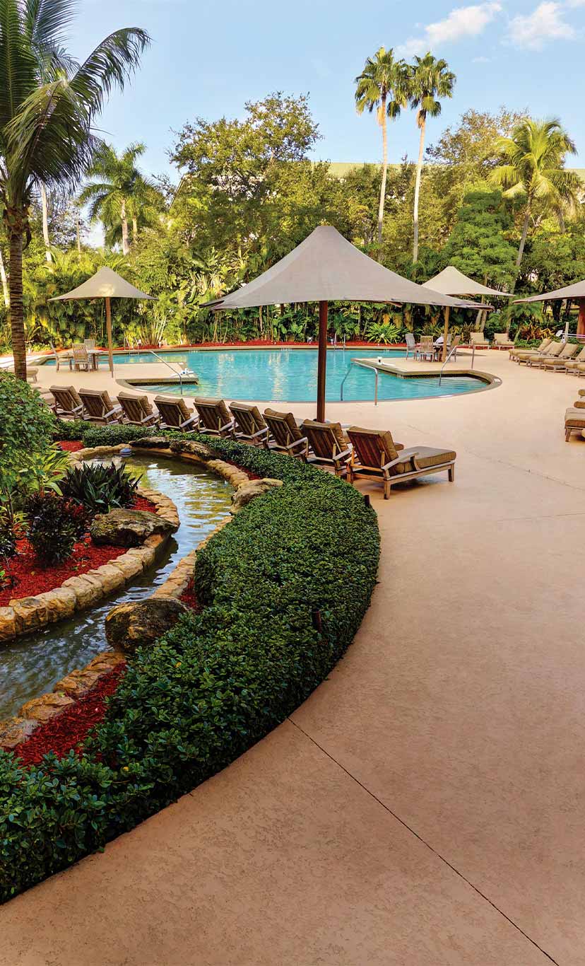 Outdoor pool deck with lush gardens, lounge chairs, and umbrellas