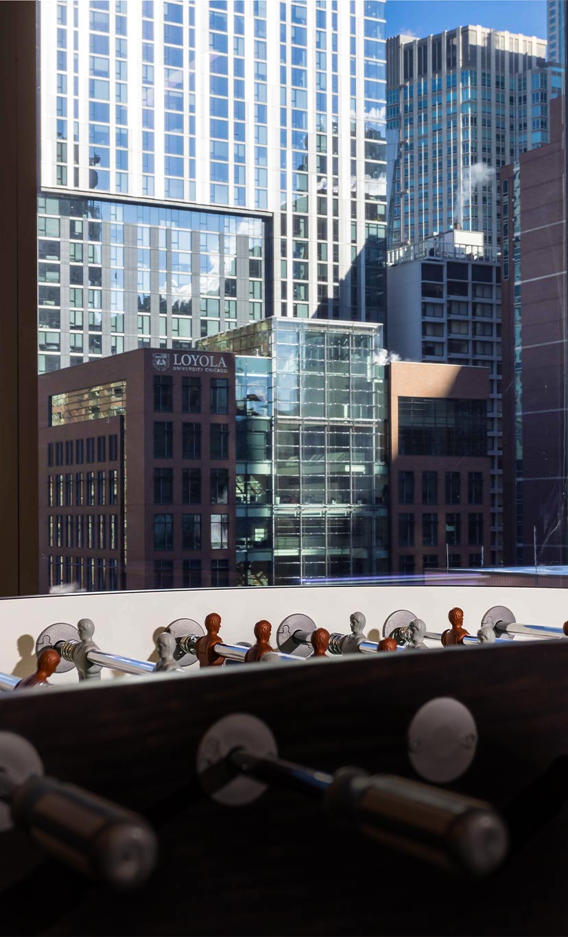 a foosball table sits next to large windows showing a city skyline