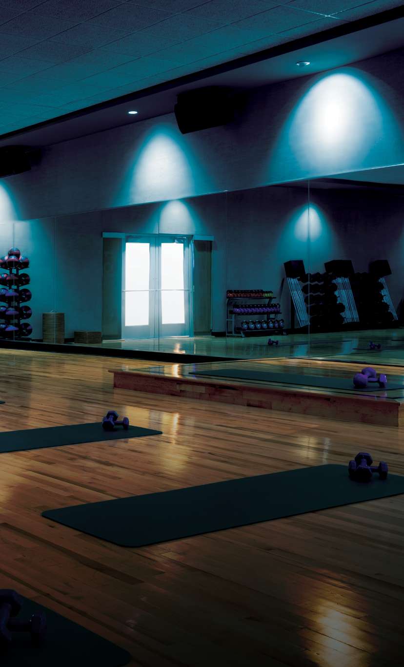 A dimly lit fitness studio with yoga mats and dumbbells laid out in a row