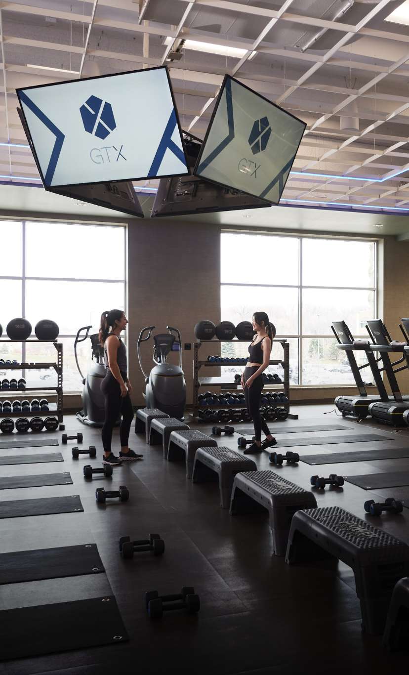 2 women laugh in a team training area with treadmills