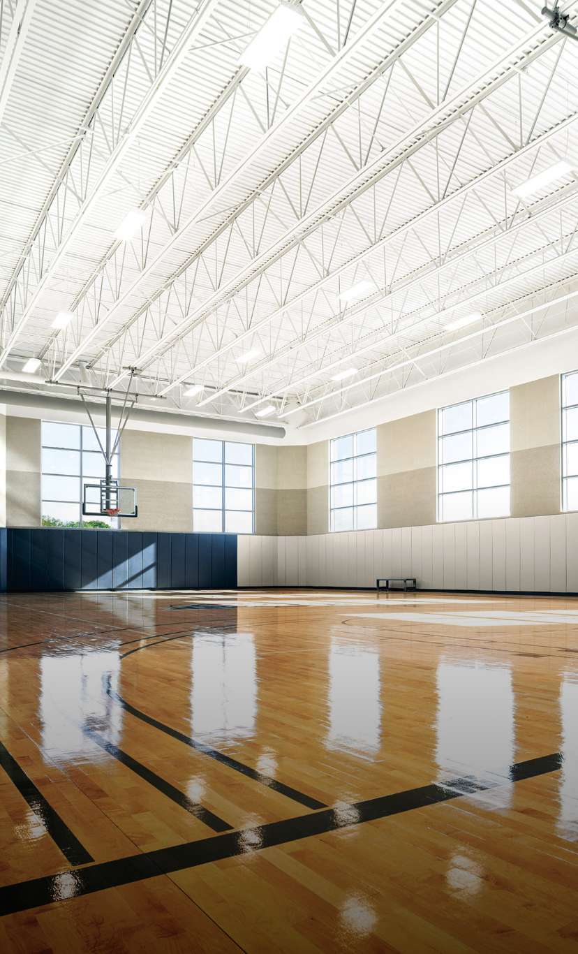 sunlight reflects off a glossy floor of an indoor basketbal court and gymnasium