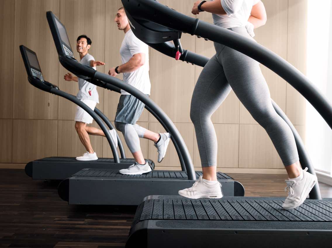 A woman and two men jog on side-by-side treadmills.