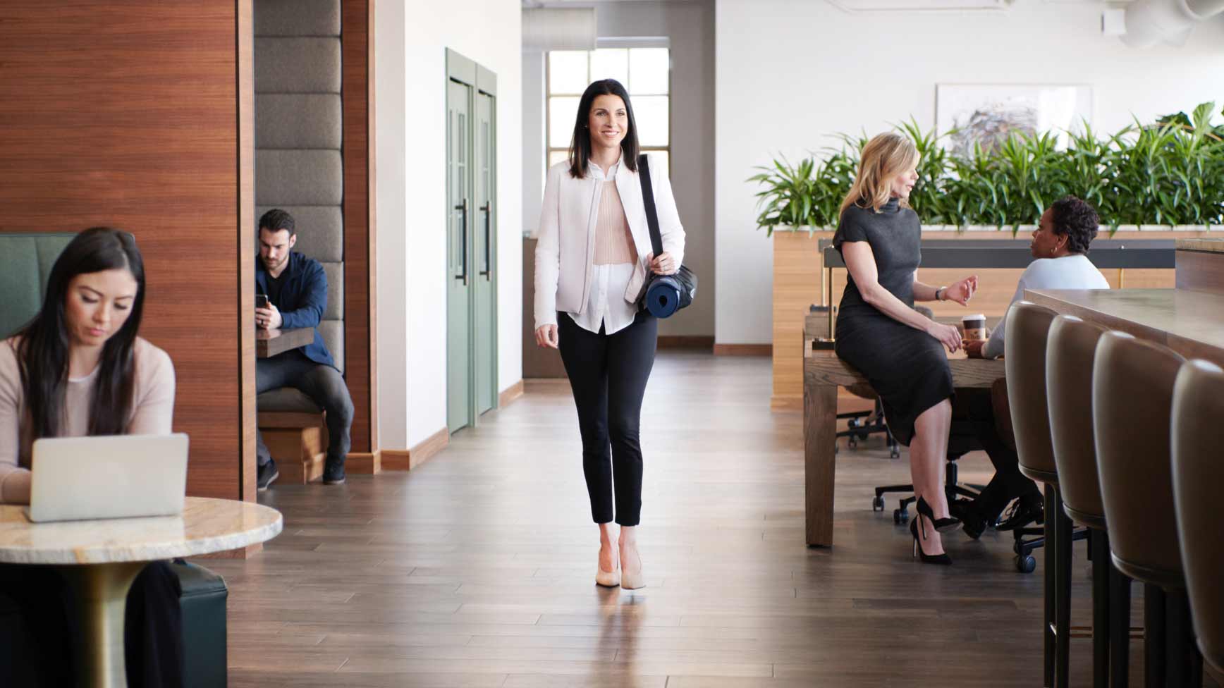 Woman walking down a hall at Life Time Work while others work at tables