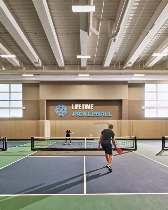 A woman receives coaching for tennis at an indoor tennis court at Life Time