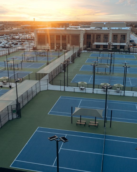 Outdoor tennis courts by the life time frisco building with a setting sun.