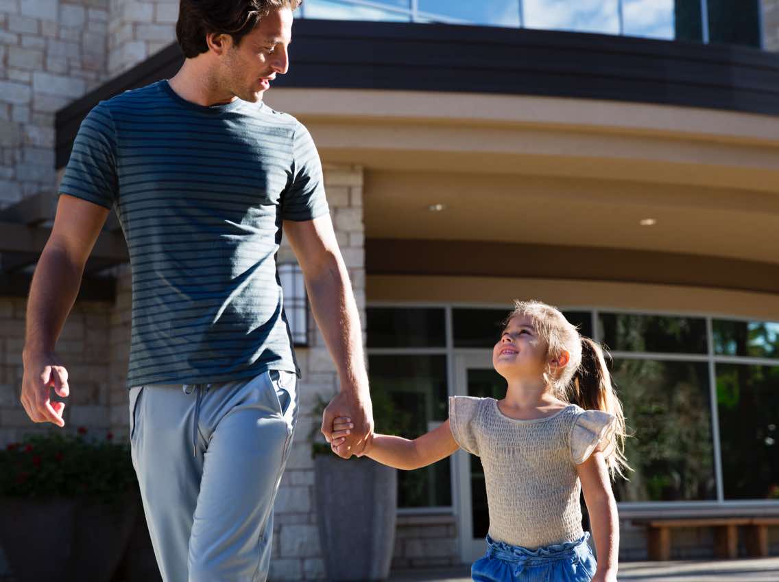 Man holding hands with a female child while walking out of Life Time