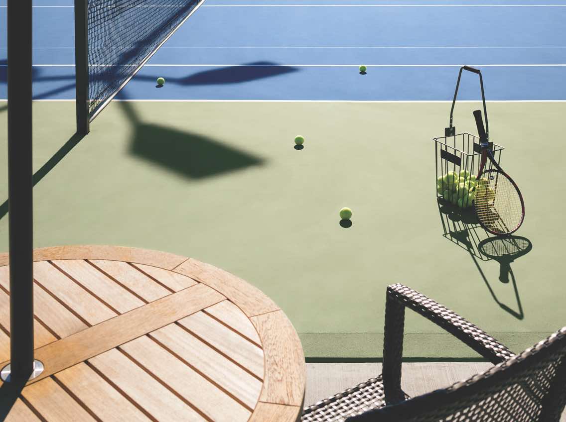 Close view of a basket of tennis balls and tennis racquet on an outdoor tennis court