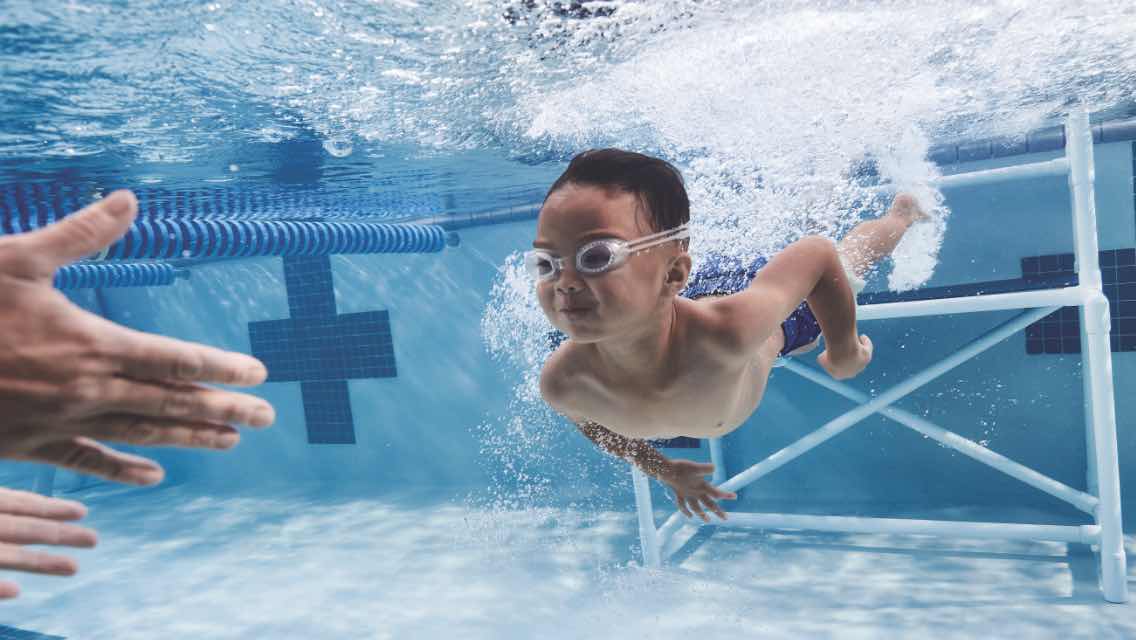 Little boy swimming underwater during swimming lessons at Life Time.