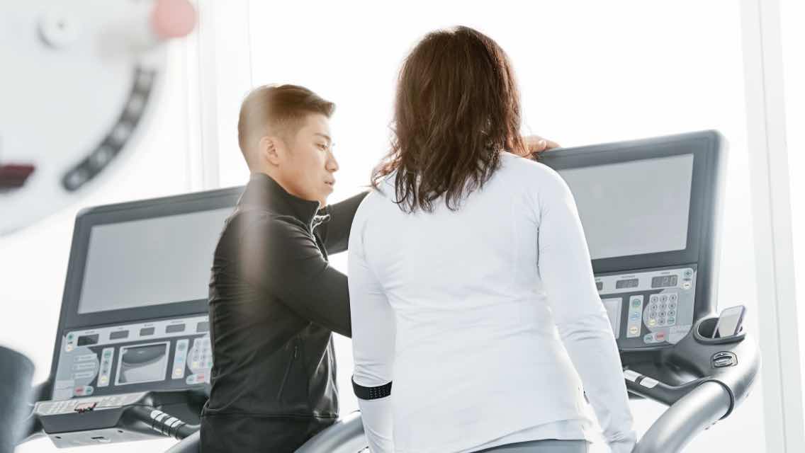 Personal trainer helping a female member on a treadmill during a personal training session.