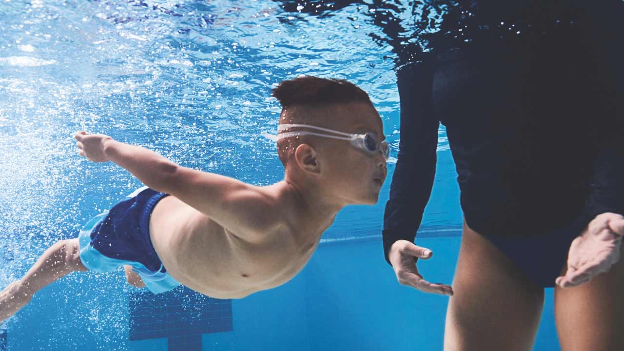 A young boy swimming alongside an instructor at the Life Time pool