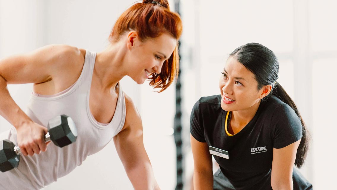 A woman lifting weights with a personal trainer at Life Time