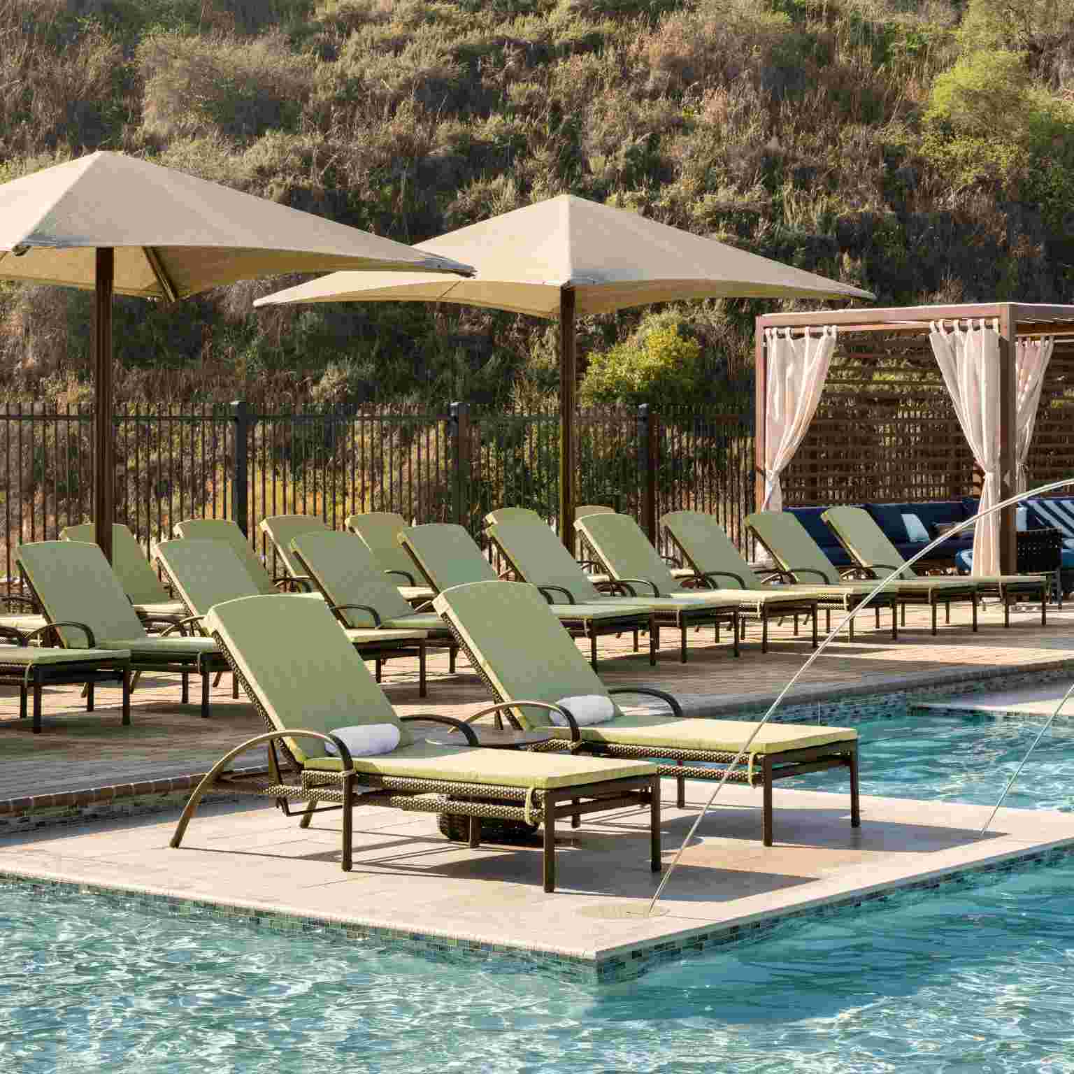 rows of beach loungers and cabanas surround a sparkeling pool with water features.
