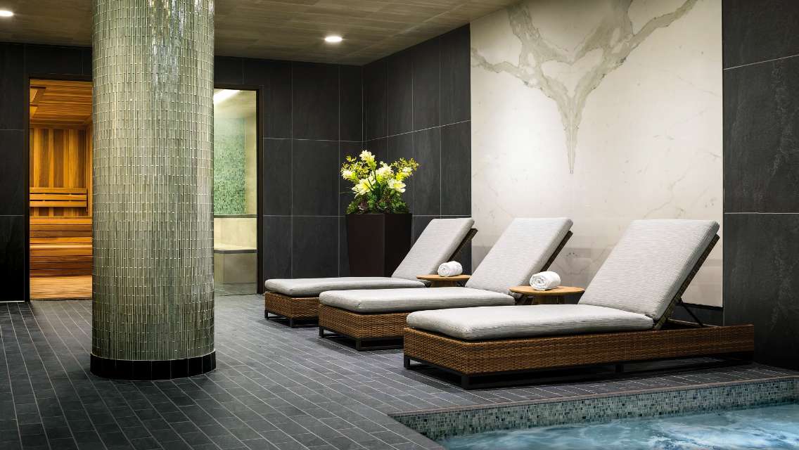 An architectural shot of an indoor whirlpool, lounging chairs, a steam room and sauna. 